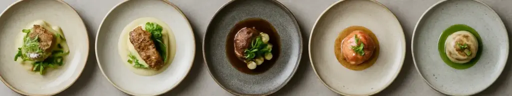 Seks nordiske gourmetanretninger på grå keramik side om side, set lige ovenfra.