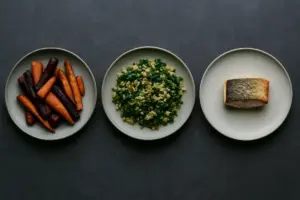 Tre tallerkener side om side: rodfrugter, korn og grønt, og en lille portion fisk.