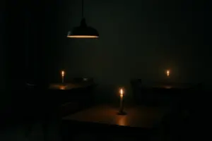 Dæmpet oplyst spisesal med et enkelt stearinlys på hvert bord og en lav pendel over.