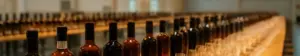 Lange borde med flasker med rom, whisky, portvin og cognac samt rækker af smagsglas i en hal