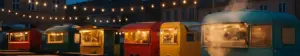 Madboder og langborde med lyskæder på en bytorv til streetfoodfestival i skumringen