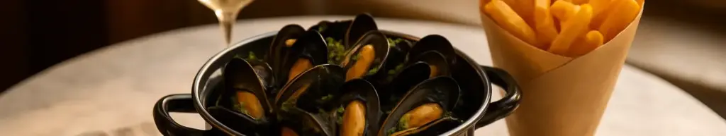 Gryde med dampede blåmuslinger, pommes frites og et glas hvidvin på et bistrobord