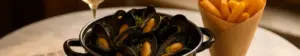 Gryde med dampede blåmuslinger, pommes frites og et glas hvidvin på et bistrobord